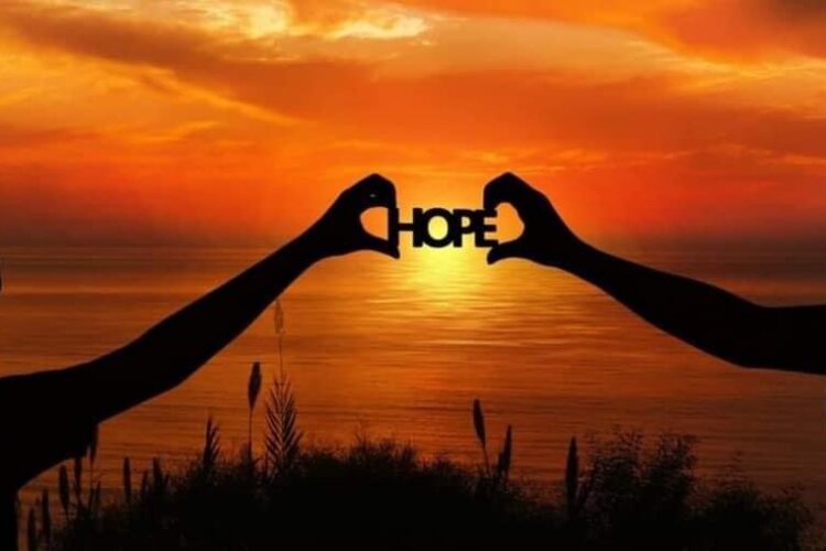 two people holding up the word hope in front of a sunset